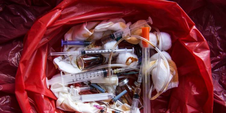 The contents of a bright red hazardous medical waste bag reveal used syringes, bandages, tubes, and ampoules.