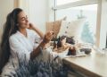 A young woman adding essential oils to a home diffuser. She has a lavender plant, a candle, and pillows near her.