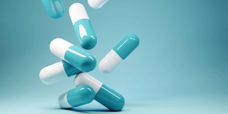 Eight turquoise and white pill capsules cascade down the frame. The background starts with a dark turquoise and becomes lighter.