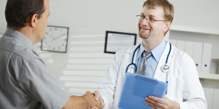 Medical office - middle-aged male doctor greeting patient, shaking hands.