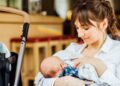 A young mother holding her infant at a dining table in public. She's confidently breastfeeding with the stroller next to her.