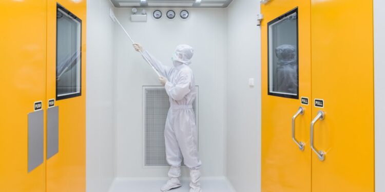 An individual wearing a white sterile gown and gloves is using a cleaning tool to scrub a white wall.